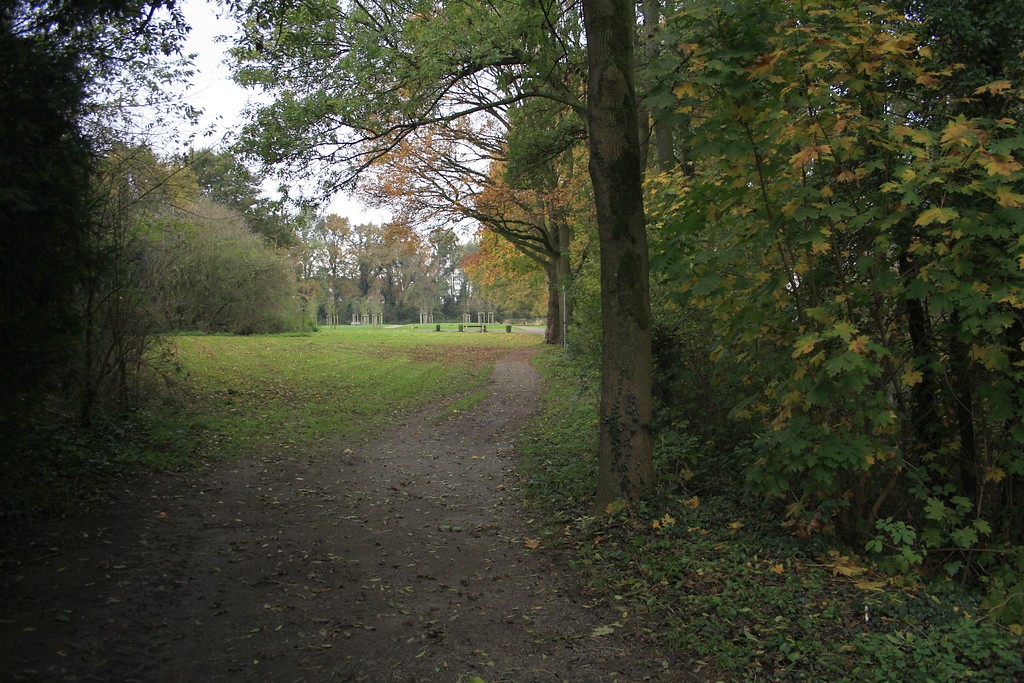 Ein Weg durch den Park an der Wasserburg Haus Voerde an der Allee in Voerde. Die Grünfläche ist gesäumt von alten Laubbäumen. Rechts liegen die Gräfte und die Burg (2014).