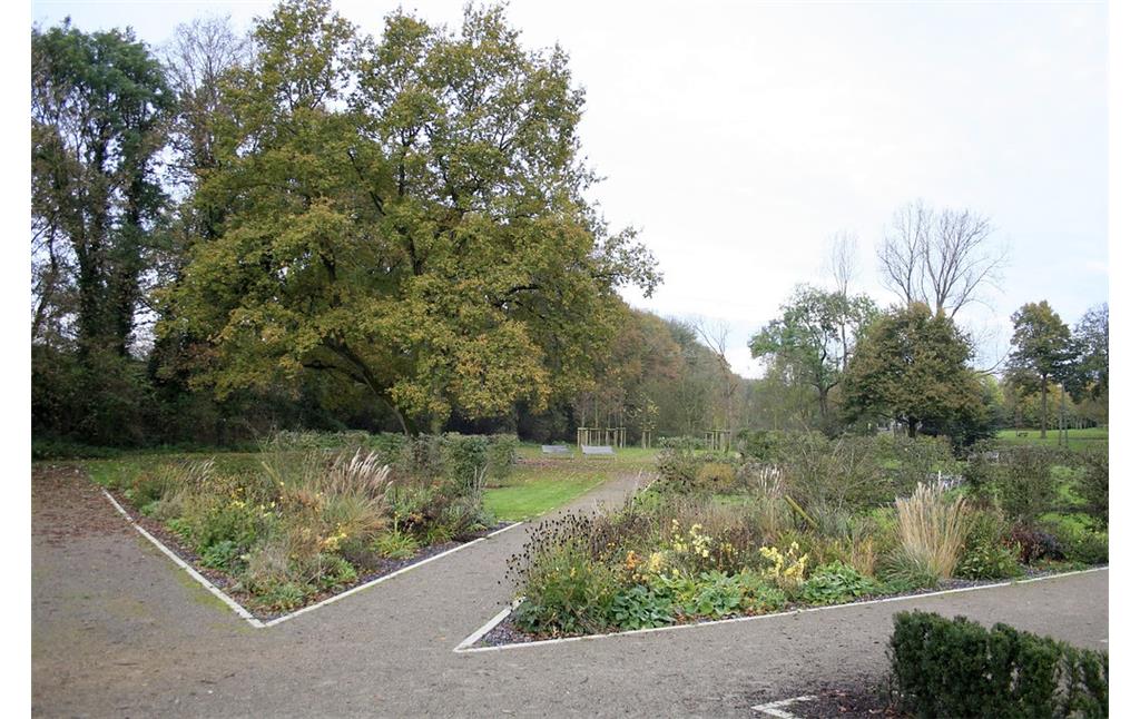 Ein kleiner Park an der Wasserburg Haus Voerde an der Allee in Voerde. Blumenbeete, Sitzbänke und Bäume stehen eingestreut zwischen Rasenflächen und Wegen (2014).