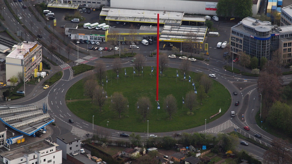 Der Potsdamer Platz in Bonn, Endpunkt der Bundesautobahn A 555 (2014). Links das Hauptgebäude von "Verpoorten" und auf der Grünfläche eine rote Stahl-Stele der "Regionale 2010".