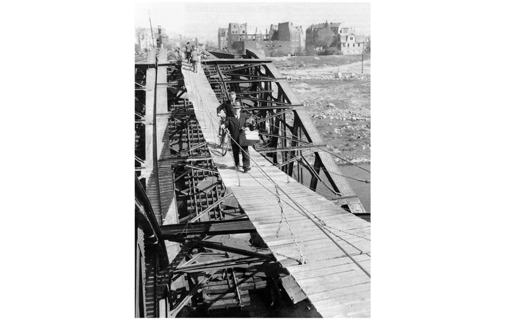 Koblenzer Einwohner passieren am 26. April 1945 die vom 372. Pionier-Regiment der US-Armee über der schwer beschädigten Moseleisenbahnbrücke errichtete Hängebrücke.