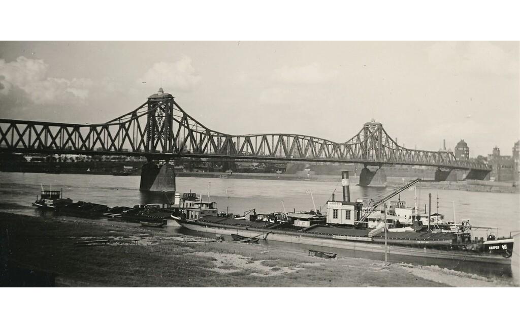 Historische Aufnahme der 1945 zerstörten Admiral-Scheer-Brücke zwischen den Duisburger Stadtteilen Homberg und Ruhrort über den Rhein (1941), im Vordergrund fährt ein Frachtschiff.