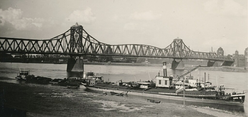 Historische Aufnahme der 1945 zerstörten Admiral-Scheer-Brücke zwischen den Duisburger Stadtteilen Homberg und Ruhrort über den Rhein (1941), im Vordergrund fährt ein Frachtschiff.